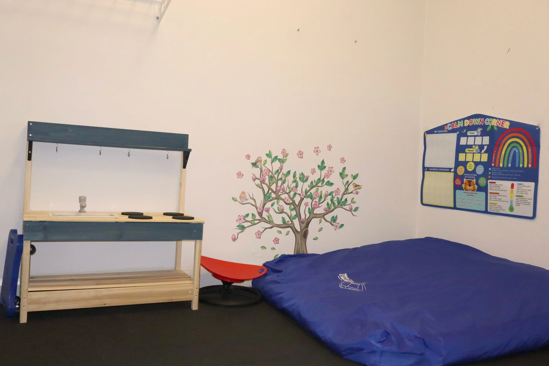 Sensory calm down corner at Square One with mud kitchen, spinning seat, crash mat and calm down corner visual chart used during occupational therapy sessions