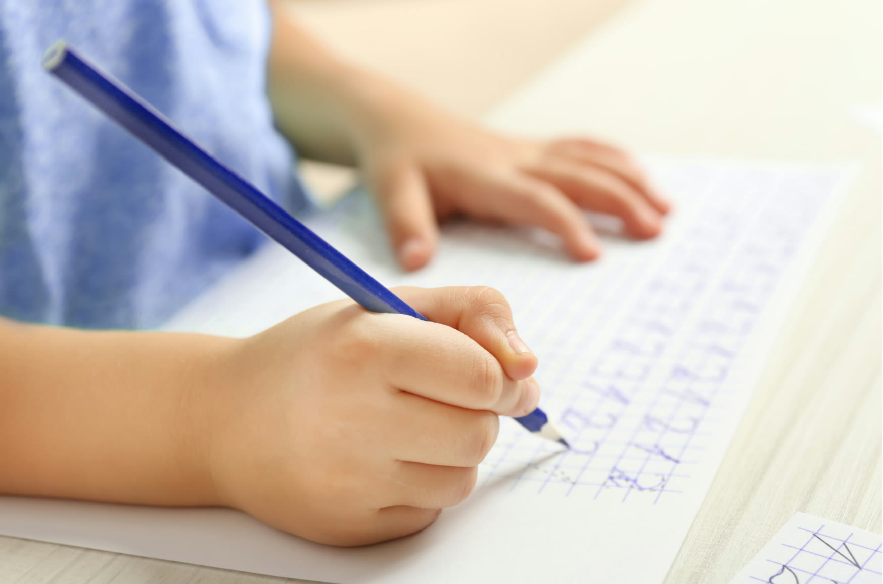 Young child gripping a pencil while practising letter formation in a handwriting workbook